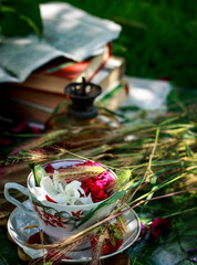 Summer composition, cup with peony petals, oil lamp, old books, wheat on a sunny day