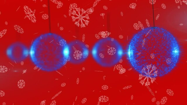 Snowflakes falling over multiple blue christmas bauble hanging decorations against red background