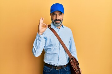 Middle age man with beard and grey hair wearing delivery courier cap smiling positive doing ok sign with hand and fingers. successful expression.