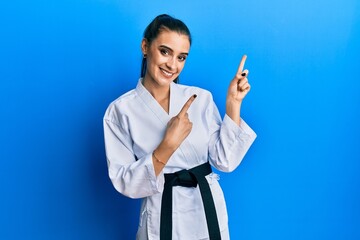Beautiful brunette young woman wearing karate fighter uniform with black belt smiling and looking...