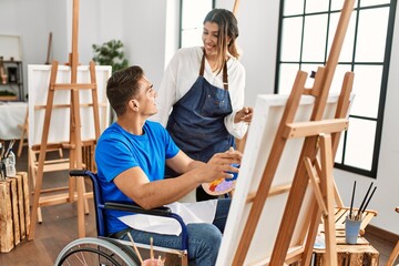 Teacher and disabled paint student sitting on wheelchair smiling happy painting at art school.