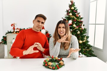 Young hispanic couple sitting at the table on christmas disgusted expression, displeased and fearful doing disgust face because aversion reaction. with hands raised