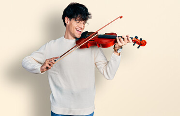 Handsome hipster young man playing violin smiling and laughing hard out loud because funny crazy...