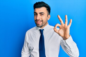Young hispanic man wearing business clothes smiling positive doing ok sign with hand and fingers. successful expression.