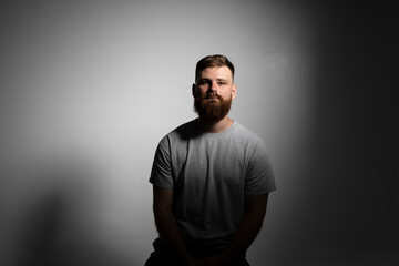 Fototapeta premium Close-up portrait of a handsome a brunette brutal bearded man in a grey t-shirt. Stylish and handsome man with a beard.