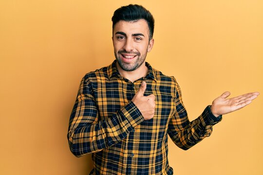 Young hispanic man wearing casual clothes showing palm hand and doing ok gesture with thumbs up, smiling happy and cheerful