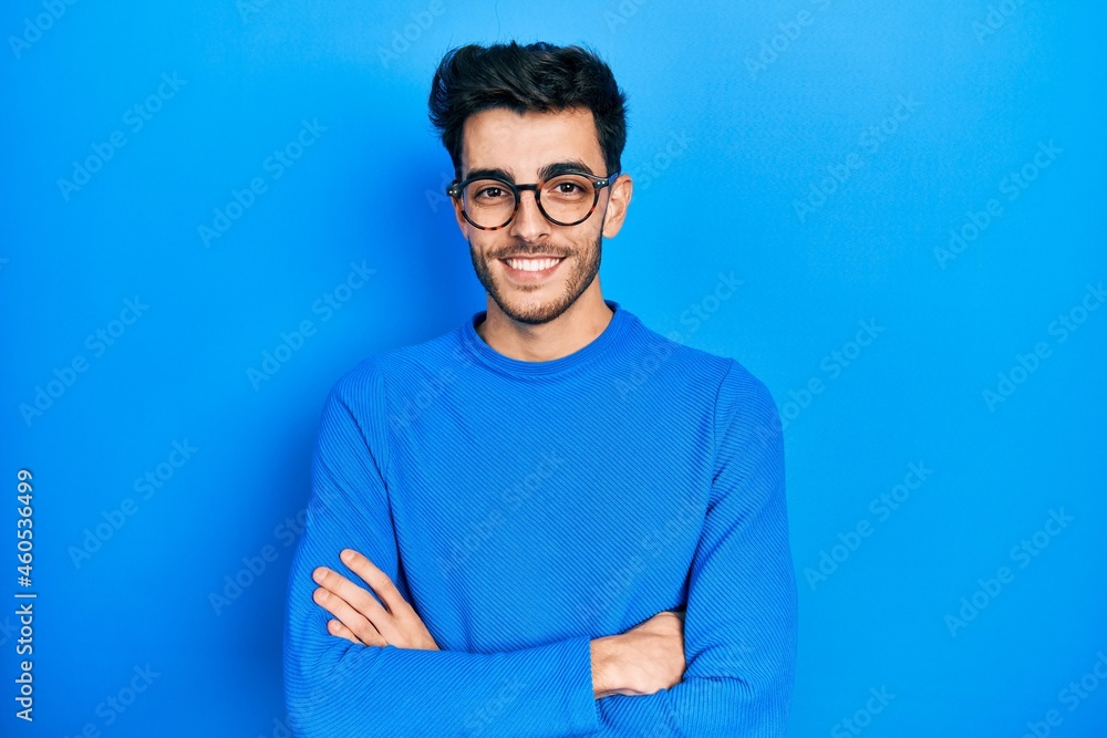 Wall mural Young hispanic man wearing casual clothes and glasses happy face smiling with crossed arms looking at the camera. positive person.