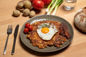 Rösti Teller mit Ei undSpeck auf Holztisch und Gemüse.