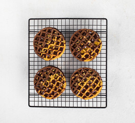 Vegan round viennese cocoa pumpkin waffles with chocolate sauce and walnuts on a metal stand on a white background