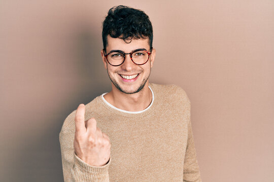 Young hispanic man wearing casual clothes and glasses beckoning come here gesture with hand inviting welcoming happy and smiling