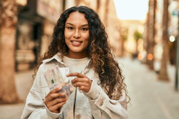 Young latin woman smiling happy counting colombia pesos banknotes at the city.