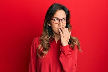 Young latin woman wearing casual clothes and glasses looking stressed and nervous with hands on mouth biting nails. anxiety problem.