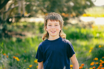 Boy with mullet hairstyle outdoors with wildflowers and long grass