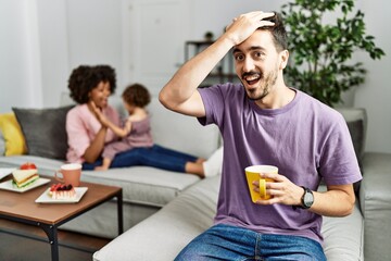 Hispanic father of interracial family drinking a cup coffee surprised with hand on head for...