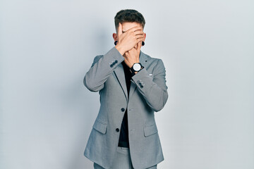 Young caucasian boy with ears dilation wearing business jacket covering eyes and mouth with hands, surprised and shocked. hiding emotion
