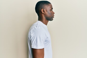 Young african american man wearing casual white t shirt looking to side, relax profile pose with...