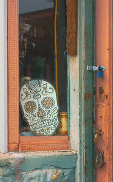 Store window display of Day of the dead skeleton head. It is placed by an old locked door. This celebration occurs in Mexico