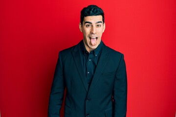 Handsome hispanic man wearing business clothes sticking tongue out happy with funny expression. emotion concept.