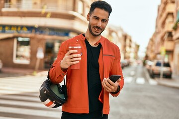 Young hispanic man using smartphone drinking coffee helmet at the city.