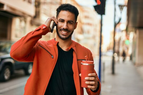 Young hispanic man talking on the smartphone drinking coffee at the city.