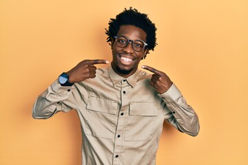 Young african american man wearing casual clothes and glasses smiling cheerful showing and pointing with fingers teeth and mouth. dental health concept.