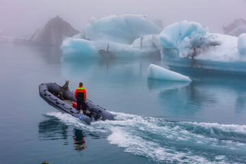 A rescue staff with a rescue dog riding a rubber patrol boat in the frigid waters and ice beg laden...