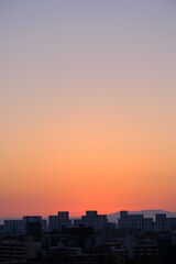 都市の夜明け、早朝ビルの隙間から太陽が昇り辺りはオレンジ色に染まる。ビルはシルエットに浮かぶ