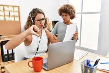 Young business mother working at the office with kid with angry face, negative sign showing dislike with thumbs down, rejection concept
