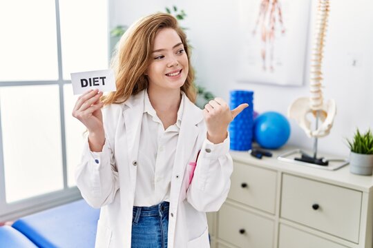 Young caucasian woman working at rehabilitation clinic holding diet banner pointing thumb up to the side smiling happy with open mouth