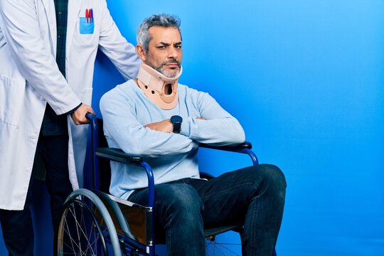Handsome middle age man with grey hair on wheelchair wearing cervical collar skeptic and nervous, disapproving expression on face with crossed arms. negative person.