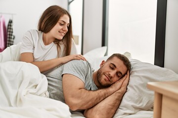 Obraz na płótnie Canvas Young caucasian woman looking her sleepy boyfriend at bed.
