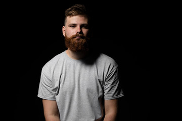 Obraz premium Close-up portrait of a handsome a brunette brutal bearded man in a grey t-shirt. Stylish and handsome man with a beard.