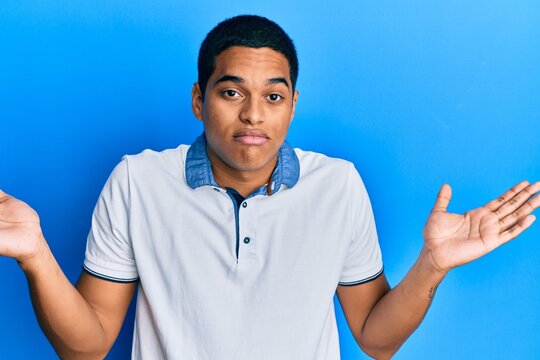 Young handsome hispanic man wearing casual clothes clueless and confused with open arms, no idea and doubtful face.