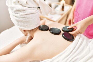 Woman reciving back massage with black stones at beauty center.