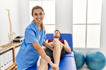 Fototapeta premium Young hispanic physioterapist woman make ankle rehab treatment to man at the clinic.