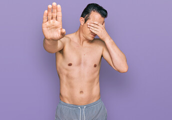 Fototapeta premium Handsome young man wearing swimwear shirtless covering eyes with hands and doing stop gesture with sad and fear expression. embarrassed and negative concept.