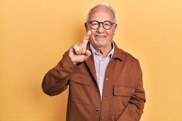 Senior man with grey hair wearing casual jacket and glasses showing and pointing up with finger number one while smiling confident and happy.