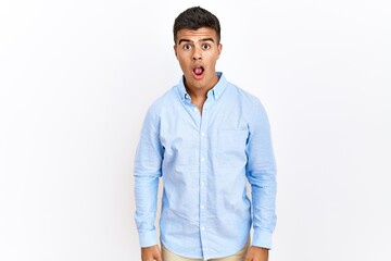 Young hispanic man wearing business shirt standing over isolated background afraid and shocked with surprise and amazed expression, fear and excited face.