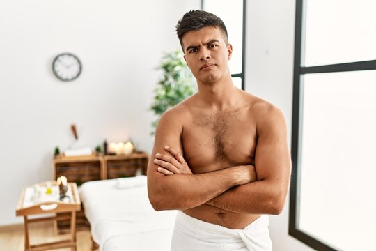 Young hispanic man standing shirtless at spa center skeptic and nervous, disapproving expression on face with crossed arms. negative person.