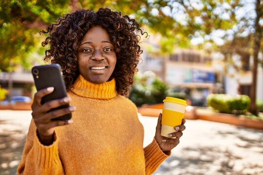 African american woman using smartphone drinking coffee at park