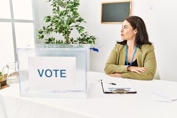 Young brunette woman sitting at election table with voting ballot looking to side, relax profile...
