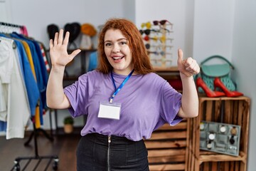 Young redhead woman working as manager at retail boutique showing and pointing up with fingers number six while smiling confident and happy.