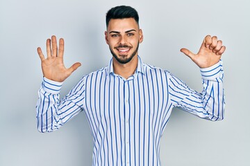 Young hispanic man with beard wearing casual striped shirt showing and pointing up with fingers number six while smiling confident and happy.