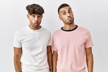 Young gay couple standing over isolated background making fish face with lips, crazy and comical gesture. funny expression.