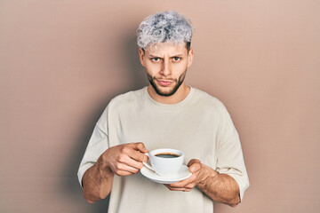 Young hispanic man with modern dyed hair drinking a cup of coffee skeptic and nervous, frowning upset because of problem. negative person.