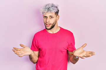 Young hispanic man with modern dyed hair wearing casual pink t shirt clueless and confused with...