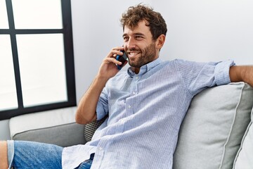 Young hispanic man talking on the smartphone sitting on the sofa at home.