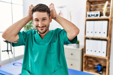 Young physiotherapist man working at pain recovery clinic doing bunny ears gesture with hands palms looking cynical and skeptical. easter rabbit concept.