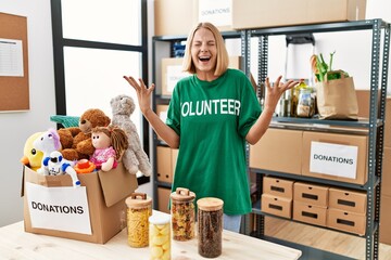 Young caucasian woman wearing volunteer t shirt at donations stand celebrating mad and crazy for...