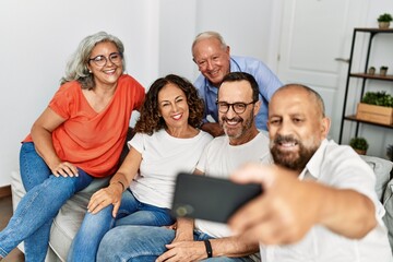 Group of middle age friends smiling happy make selfie by the smartphone at home.